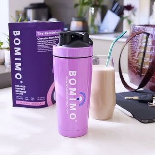 The Bomimo protein shaker in front of a packet of The Menoshake and a glass of the chocolate protein shake next to a handbag, car keys and an ipad.